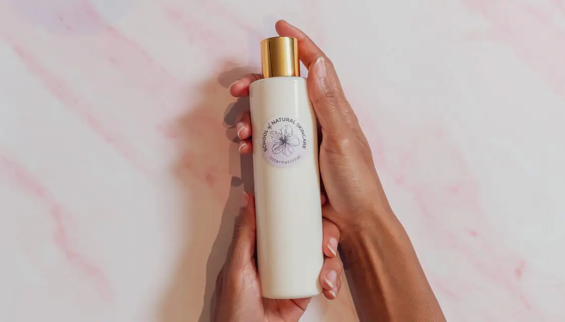 Hands holding skincare lotion bottle.
